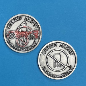 May include: Two silver-colored round coins with the text "ARRIVE ALIVE!" and "Don't Text and Drive." One coin features a red car with glitter and a phone symbol crossed out. The other coin has a phone symbol crossed out.