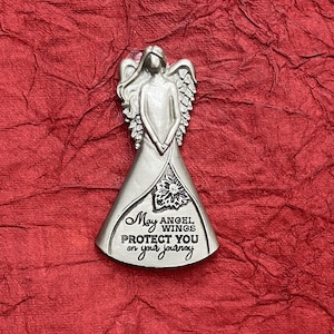 May include: A silver angel figurine with outstretched wings, set against a textured red background. The angel's dress features a floral design and the inscription "May angel wings protect you on your journey."