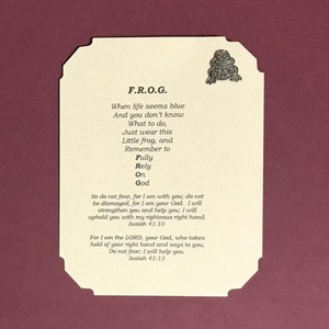May include: A white card with a blue frog pin on top. The card has the acronym F.R.O.G. and a poem about relying on God. The poem includes the Bible verses Isaiah 41:10 and Isaiah 41:13.