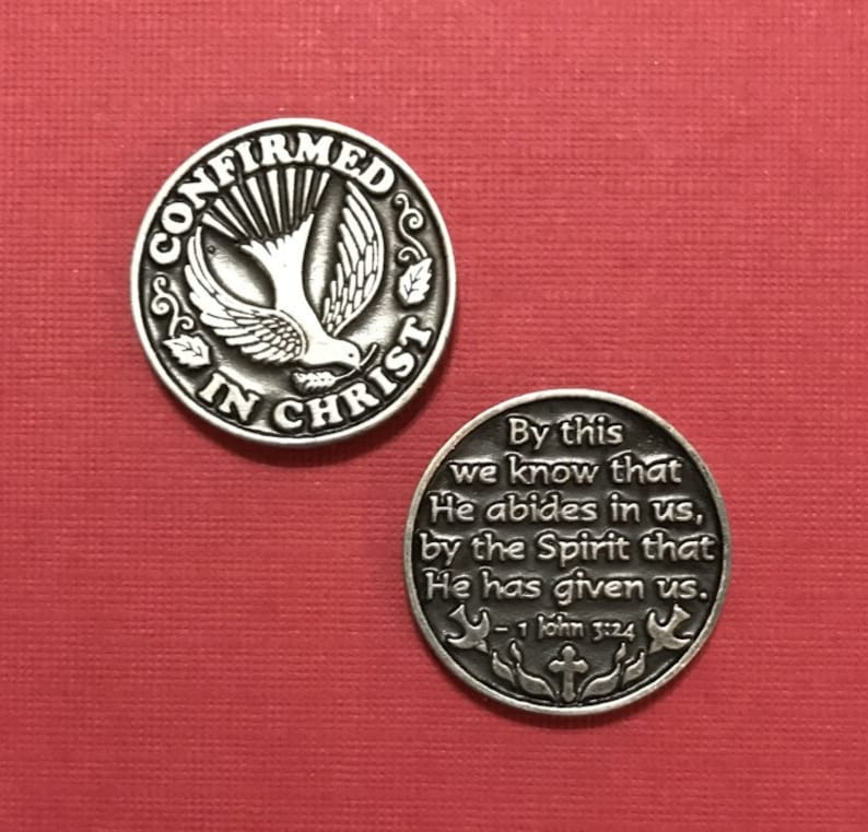 K&ouml;nnte beinhalten: Silberfarbener Metall-Token mit einer Taube und den Worten "Best&auml;tigt in Christus". Auf der R&uuml;ckseite des Tokens befindet sich ein Vers aus der Bibel: "Daran erkennen wir, dass er in uns wohnt: durch den Geist, den er uns gegeben hat. -1 Johannes 3:24"