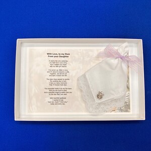 Puede incluir: Un pa&ntilde;uelo blanco con borde de encaje, un peque&ntilde;o dije de &aacute;ngel plateado y un lazo de cinta morada clara, presentado en una caja blanca junto a una tarjeta impresa con el texto: With Love, to my Mom From your Daughter, seguido de un poema.
