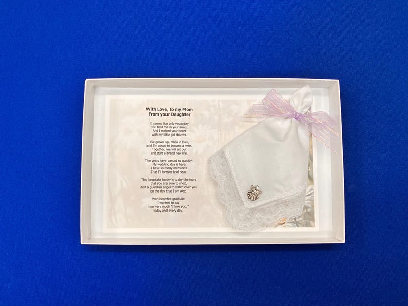 Puede incluir: Un pa&ntilde;uelo blanco con borde de encaje, un peque&ntilde;o dije de &aacute;ngel plateado y un lazo de cinta morada clara, presentado en una caja blanca junto a una tarjeta impresa con el texto: With Love, to my Mom From your Daughter, seguido de un poema.