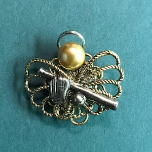 Op de afbeelding: Een gouden bedel met een honkbalknuppel, handschoen en bal. De bedel is bevestigd aan een gouden ketting met een parel.