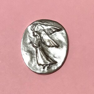 Oval pewter token with angel embossed on token with bright silver finish on the one side.