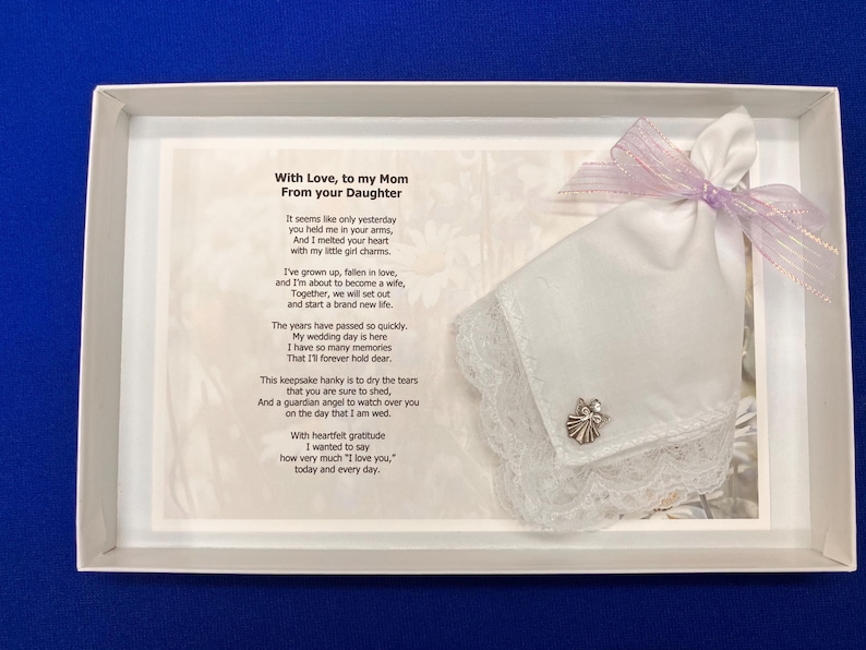 Puede incluir: Un pa&ntilde;uelo blanco con borde de encaje y un peque&ntilde;o dije de &aacute;ngel plateado, atado con una cinta morada clara, presentado en una caja blanca junto a un poema impreso titulado With Love, to my Mom From your Daughter, con un texto emotivo.