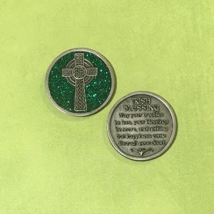 Puede incluir: Dos monedas plateadas de bendici&oacute;n irlandesa. Una moneda presenta una cruz celta sobre un fondo verde brillante. La otra moneda tiene el texto "Irish Blessing" y un verso. Las monedas est&aacute;n sobre una superficie verde claro.