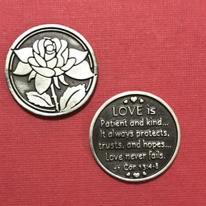 Può includere: Due monete in metallo color argento. Una moneta presenta un design a rosa dettagliato. L'altra moneta ha il testo "LOVE is Patient and kind... It always protects, trusts, and hopes... Love never fails. -1 Cor 13:4-8."