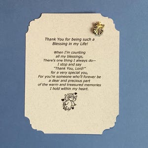 May include: A cream-colored card with a scalloped edge and the text "Thank You for being such a Blessing in my Life!". A small gold-colored angel pin is attached to the top right corner. A small angel graphic is at the bottom.
