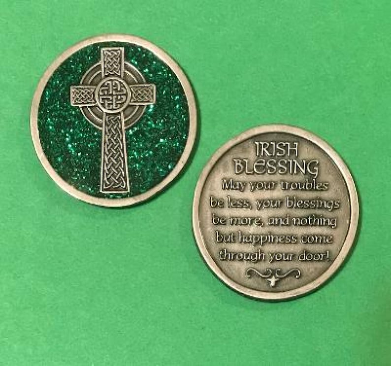 Puede incluir: Moneda irlandesa de bendici&oacute;n de dos caras. Un lado presenta una cruz celta plateada sobre un fondo verde brillante. El otro lado tiene el texto "IRISH BLESSING" y una bendici&oacute;n. La moneda es redonda con un borde plateado.