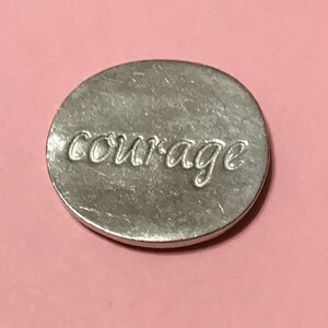 Showing the back side of the oval pewter token with  bright silver finish with the word courage engraved on it.