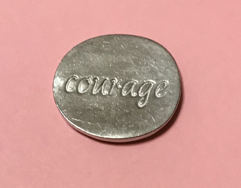 Showing the back side of the oval pewter token with  bright silver finish with the word courage engraved on it.