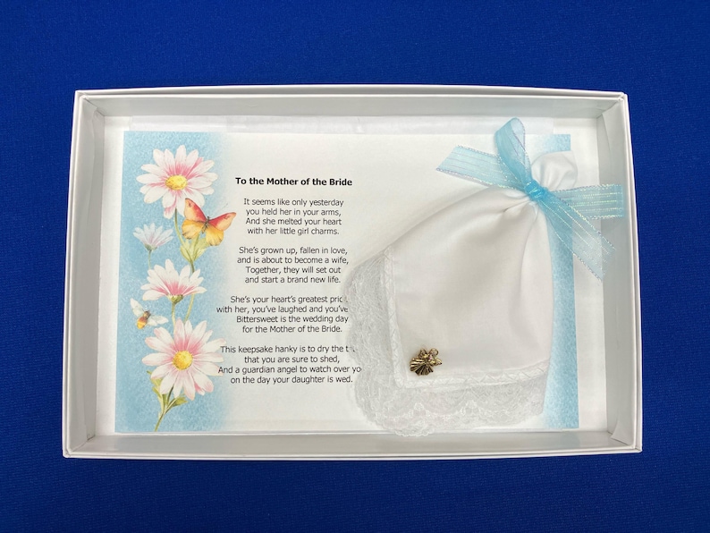 May include: A white handkerchief with lace trim and a gold charm, presented in a white box. The box contains a card with a poem and floral illustrations. A light blue ribbon adorns the handkerchief, creating a sentimental gift for the Mother of the Bride.