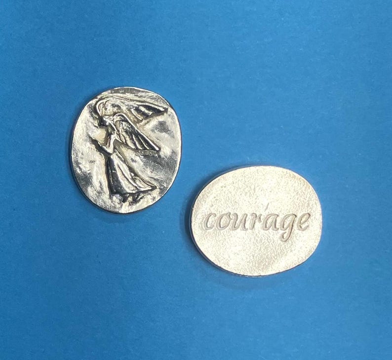 Peut inclure: Deux pendentifs argent&eacute;s sur fond bleu. L'un est ovale avec un ange. L'autre est rond avec le mot "courage" grav&eacute;. Les pendentifs sont probablement en m&eacute;tal et conviennent aux bijoux ou &agrave; l'artisanat.