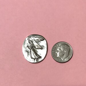 Oval pewter token with angel embossed on token with bright silver finish showing it's as wide as a dime but taller.
