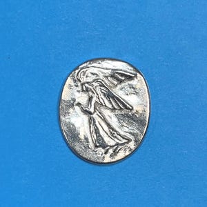 Peut inclure: Un pendentif ovale argent&eacute; repr&eacute;sentant un ange en relief avec des ailes d&eacute;ploy&eacute;es et des robes fluides. L'ange est repr&eacute;sent&eacute; dans une pose dynamique, sur un fond textur&eacute;. Le pendentif est centr&eacute; sur un fond bleu uni.