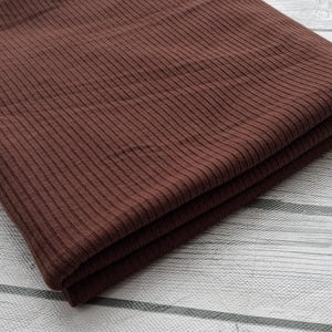 May include: A folded piece of brown ribbed fabric. The fabric has a subtle texture and a smooth finish.