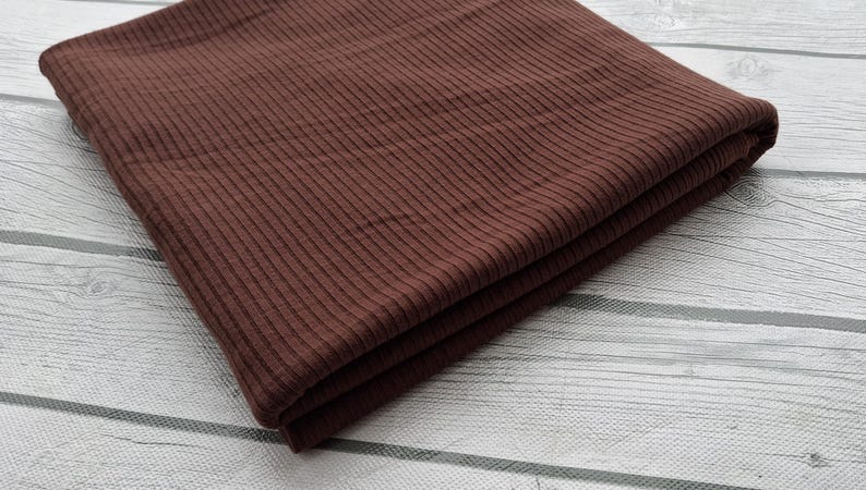 May include: A folded piece of brown ribbed fabric. The fabric has a subtle texture and a smooth finish.