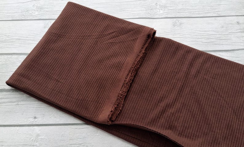 May include: A brown ribbed fabric folded in half. The fabric has a subtle sheen and a soft texture.
