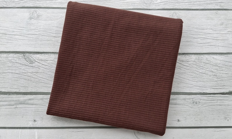 May include: A close-up of a brown ribbed fabric. The fabric has a subtle texture and a smooth finish.