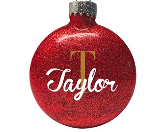 May include: Red glitter Christmas ornament with a gold letter "T" and the name "Taylor" in white cursive lettering.