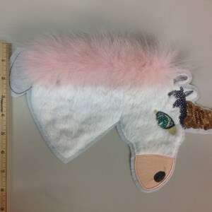 May include: White unicorn applique with a pink fur mane, a gold sequin horn, and a green eye.