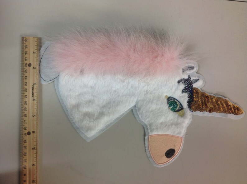 May include: White unicorn applique with a pink fur mane, a gold sequin horn, and a green eye.