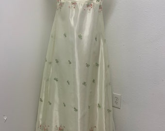 May include: A long, ivory-colored dress with a square neckline and short, puffed sleeves. The dress is adorned with delicate green and pink floral embroidery.