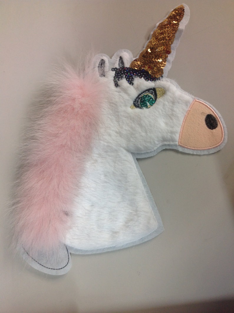 May include: White unicorn head applique with a pink fur mane, gold sequin horn, and green eye detail.