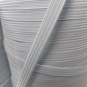 May include: A close-up of a spool of white elastic cord. The cord is wound tightly around the spool, creating a smooth, continuous surface.