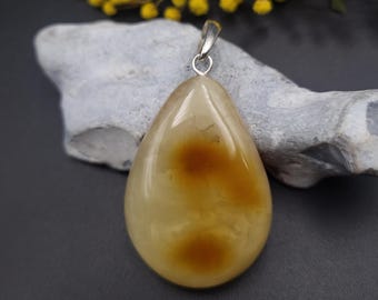 May include: A teardrop-shaped pendant made of light yellow agate with brown inclusions. The pendant is attached to a silver bail.