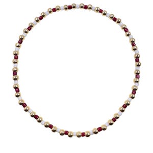 May include: A beaded bracelet featuring a circular design. The bracelet is composed of small, gold-colored, round beads interspersed with white and burgundy beads. The beads are strung together, creating a flexible and stylish accessory.