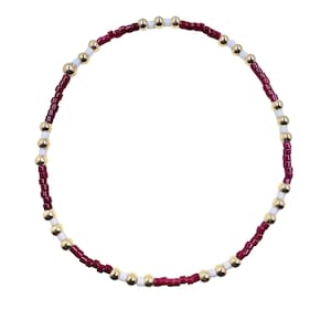 May include: A beaded bracelet featuring a circular design. The bracelet is composed of small, burgundy-colored beads, interspersed with gold and white beads. The beads are strung together, creating a flexible and stylish accessory.