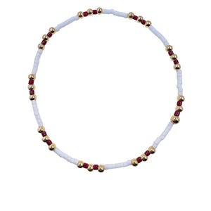 May include: A beaded bracelet featuring white, red, and gold beads. The bracelet is composed of small white rectangular beads, interspersed with red and gold spherical beads. The design is simple and elegant, suitable for everyday wear.