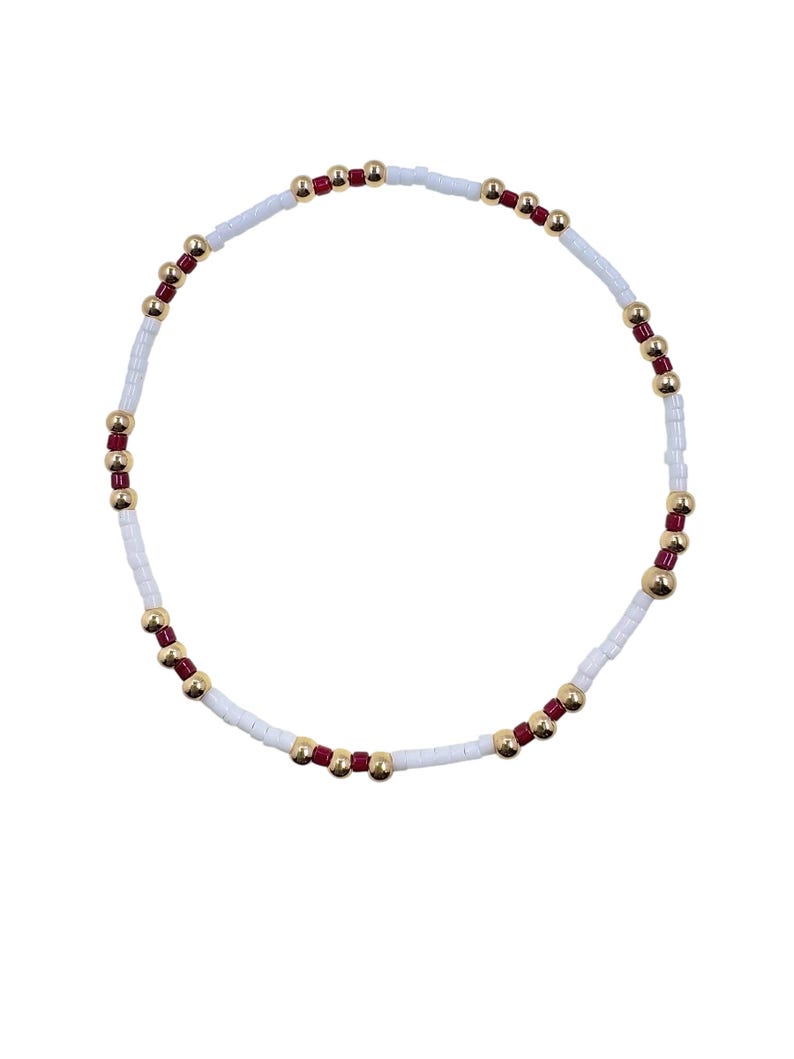May include: A beaded bracelet featuring white, red, and gold beads. The bracelet is composed of small white rectangular beads, interspersed with red and gold spherical beads. The design is simple and elegant, suitable for everyday wear.