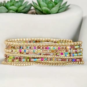 May include: A set of colorful beaded bracelets with gold accents. The bracelets are stacked on top of each other, creating a layered look.