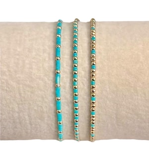 May include: Three delicate beaded bracelets. One bracelet features turquoise beads interspersed with gold-colored beads. The other two bracelets are made of gold-colored beads and turquoise beads. The bracelets are displayed on a beige surface.