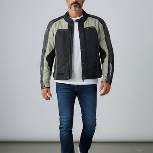 K&ouml;nnte beinhalten: Schwarze und graue Motorradjacke mit Stehkragen, getragen &uuml;ber einem wei&szlig;en T-Shirt und blauen Jeans. Die Jacke hat einen Rei&szlig;verschluss und Logos. Die Person tr&auml;gt wei&szlig;e Turnschuhe.