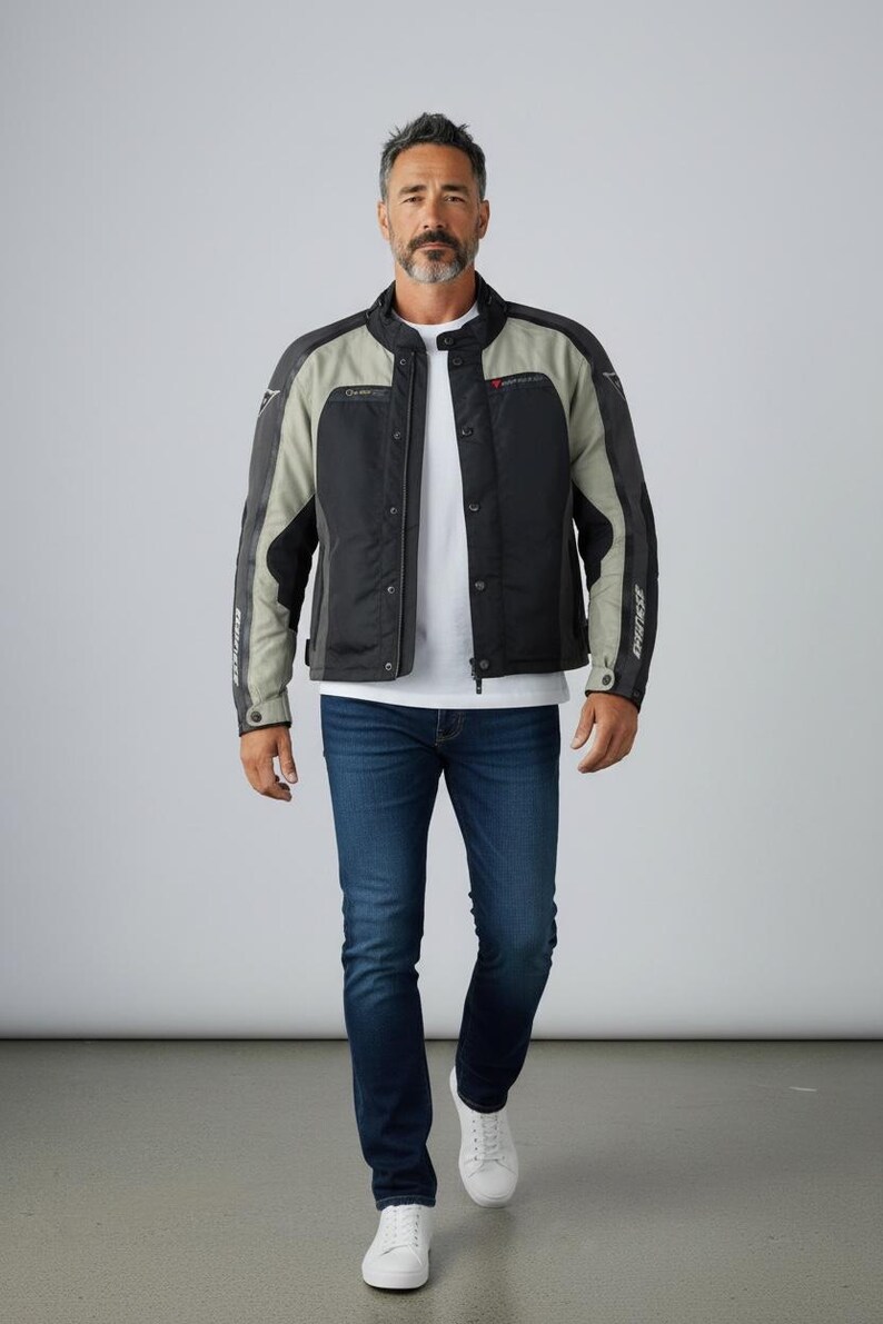 K&ouml;nnte beinhalten: Schwarze und graue Motorradjacke mit Stehkragen, getragen &uuml;ber einem wei&szlig;en T-Shirt und blauen Jeans. Die Jacke hat einen Rei&szlig;verschluss und Logos. Die Person tr&auml;gt wei&szlig;e Turnschuhe.