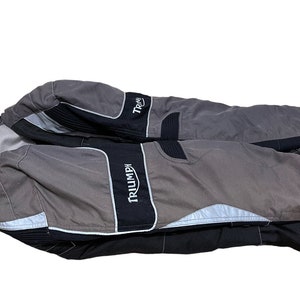 Puede incluir: Una chaqueta de moto gris y negra con la palabra "TRIUMPH" impresa en el lateral.