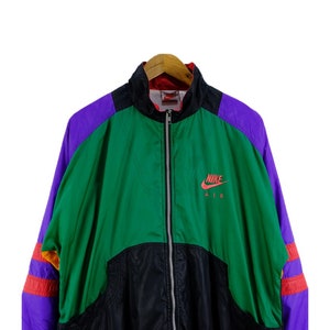 Puede incluir: Una chaqueta vintage Nike Air con un dise&ntilde;o de bloques de color negro, verde, morado y naranja. La chaqueta tiene una cremallera y un logotipo de Nike Air en el pecho.