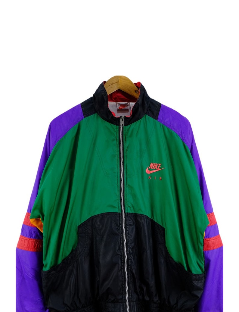 Puede incluir: Una chaqueta vintage Nike Air con un dise&ntilde;o de bloques de color negro, verde, morado y naranja. La chaqueta tiene una cremallera y un logotipo de Nike Air en el pecho.