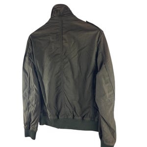 May include: Olive green bomber jacket with a ribbed collar, cuffs, and hem. The jacket has a full-length zipper and two front pockets. The back of the jacket is visible, showing the seams and construction details. A classic outerwear piece.