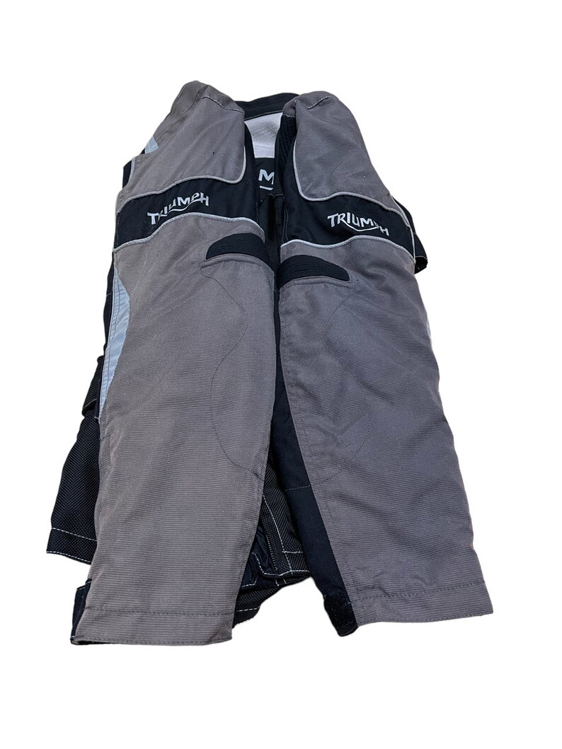 Puede incluir: Chaqueta de moto negra y gris con la palabra "Triumph" impresa en las mangas.