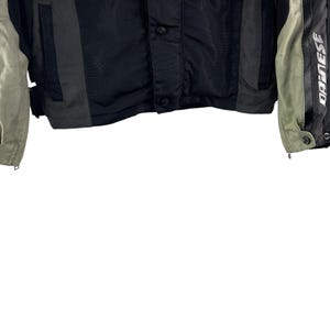 K&ouml;nnte beinhalten: Schwarze und graue Motorradjacke mit dem Wort "DAINESSE" in Wei&szlig; auf den &Auml;rmeln aufgedruckt. Die Jacke hat einen Knopfverschluss und einen Rei&szlig;verschluss an den &Auml;rmeln. Die Jacke hat graue und schwarze Eins&auml;tze.