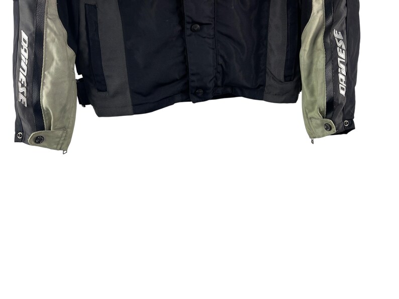 K&ouml;nnte beinhalten: Schwarze und graue Motorradjacke mit dem Wort "DAINESSE" in Wei&szlig; auf den &Auml;rmeln aufgedruckt. Die Jacke hat einen Knopfverschluss und einen Rei&szlig;verschluss an den &Auml;rmeln. Die Jacke hat graue und schwarze Eins&auml;tze.
