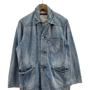 May include: A light blue denim jacket with a button closure, two chest pockets, and two large pockets on the bottom. The jacket has a faded look and is hanging on a wooden hanger.