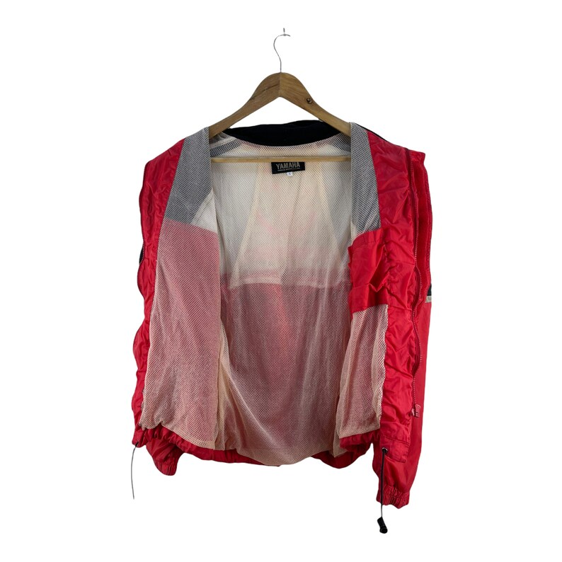 Puede incluir: Chaqueta cortavientos roja y negra con forro de malla y un logotipo de Yamaha en el interior.