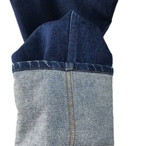 以下が含まれることがあります： 青いデニムジーンズの裾のクローズアップ。ジーンズは折り返されており、カフの中央に1本のステッチがあります。