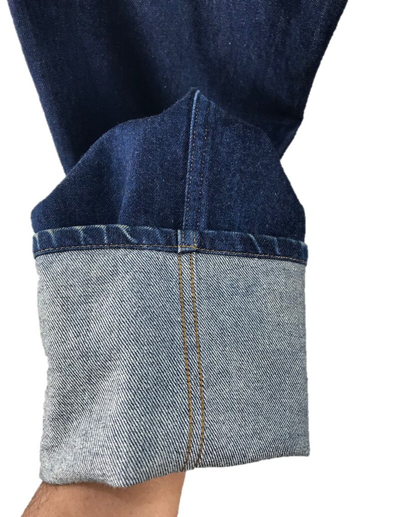 以下が含まれることがあります： 青いデニムジーンズの裾のクローズアップ。ジーンズは折り返されており、カフの中央に1本のステッチがあります。