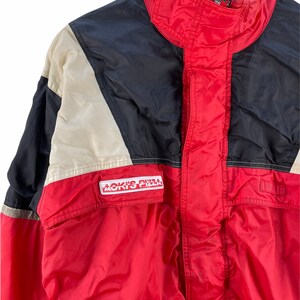 Puede incluir: Una chaqueta roja, negra y blanca con cierre de cremallera y un logotipo de "Aoki's Pizza" en la parte delantera.